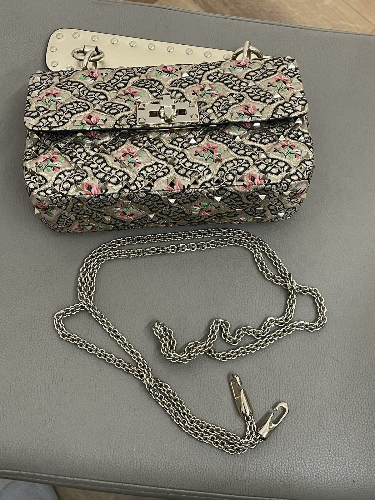 Inquadratura dall'alto della borsa Valentino Garavani Rockstud Spike Papier Floral con la tracolla a catena metallica amovibile distesa di fianco.