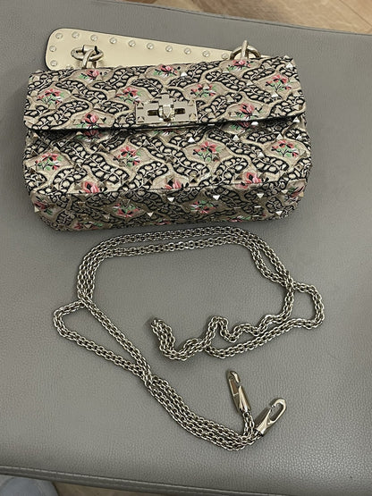 Inquadratura dall'alto della borsa Valentino Garavani Rockstud Spike Papier Floral con la tracolla a catena metallica amovibile distesa di fianco.