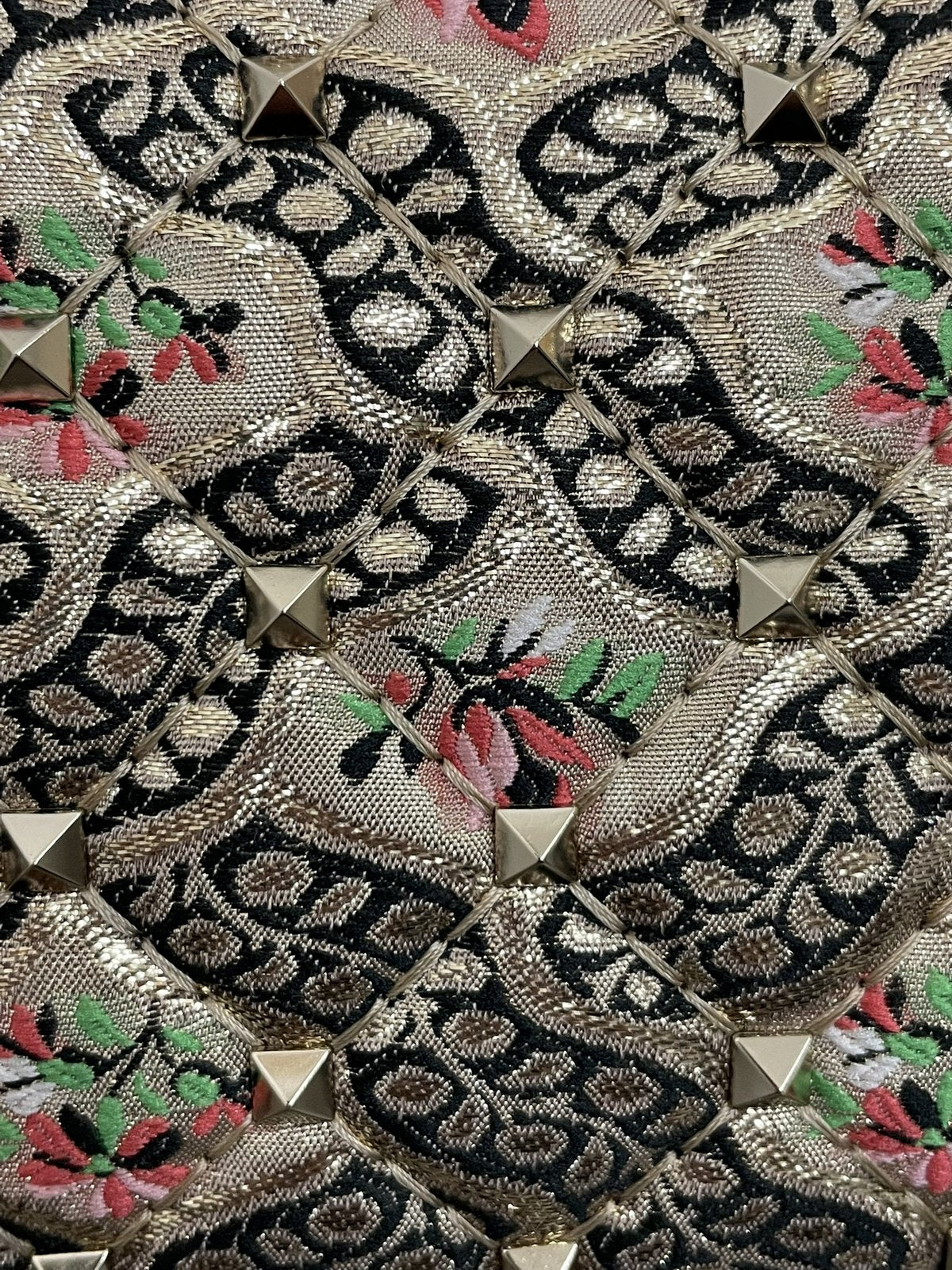 Dettaglio ravvicinato della trama del tessuto jacquard Papier Floral multicolor con ricami floreali rosa e verdi e micro-borchie piramidali applicate