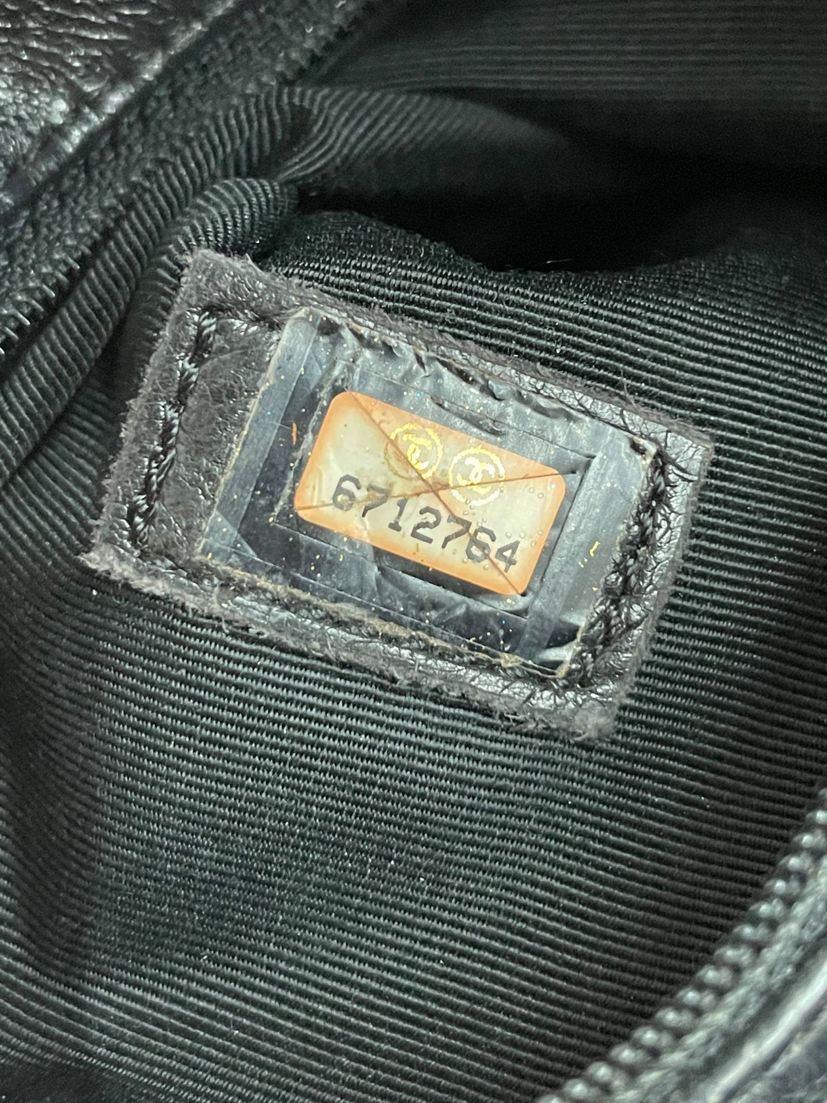 Primo piano dell'adesivo con codice seriale di autenticità Chanel situato all'interno dell'angolo della borsa