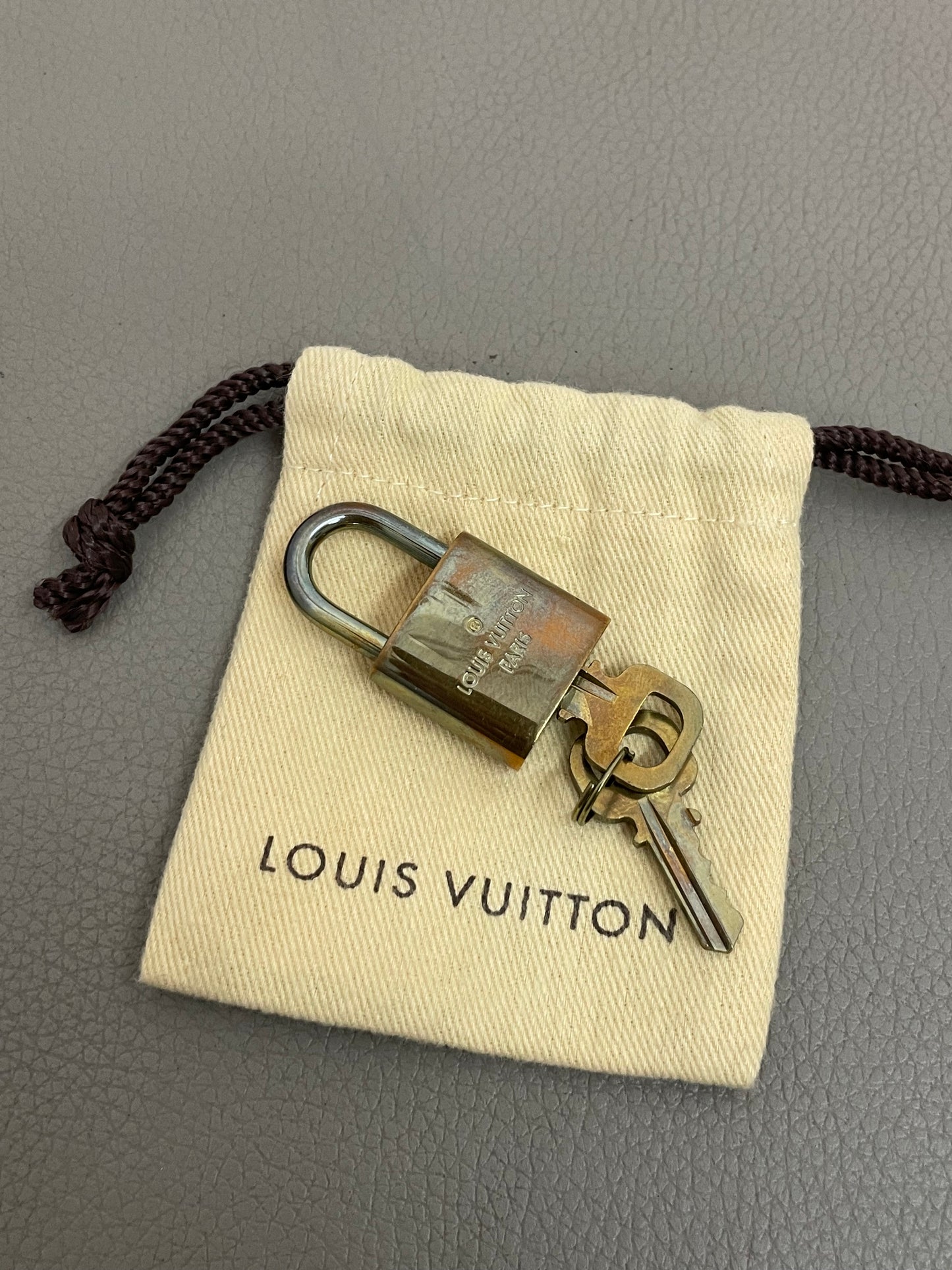 Lucchetto dorato originale Louis Vuitton con due chiavi appoggiate sul mini sacchetto antipolvere