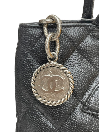 Dettaglio ravvicinato del famoso charm a medaglione argentato con logo CC inciso appeso alla cerniera della borsa Chanel